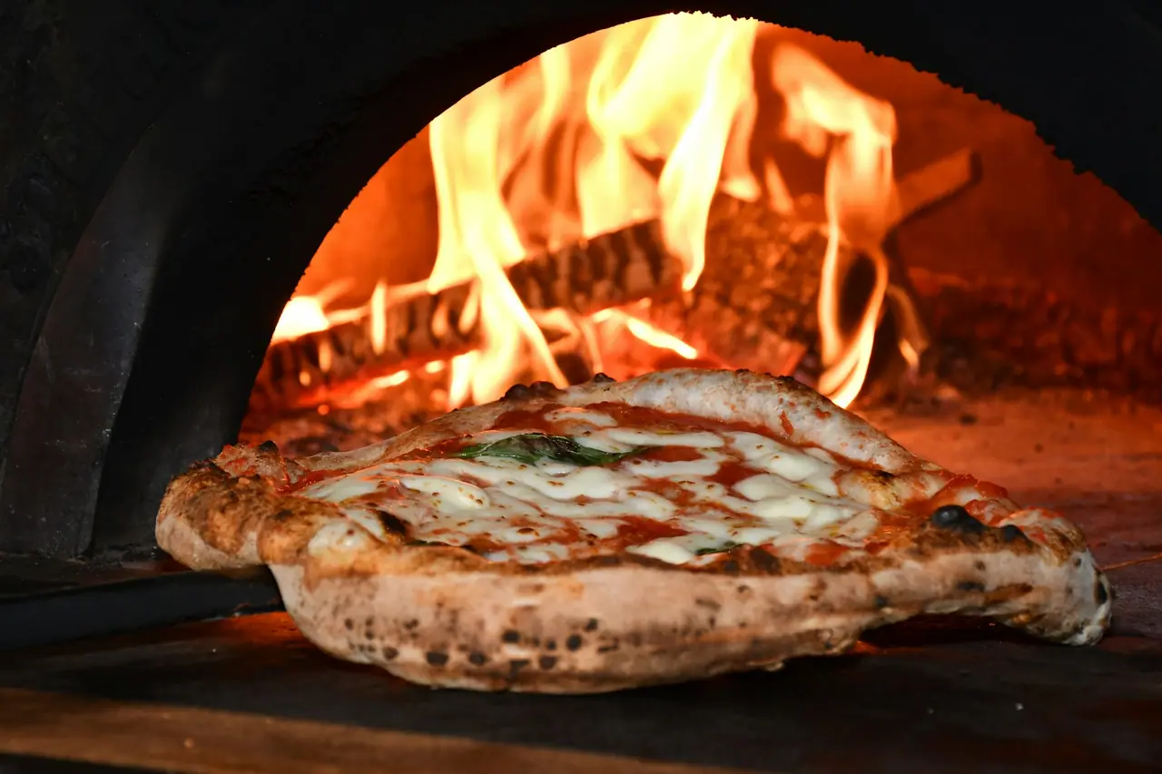 A margherita pizza baking beside the flames in the wood oven