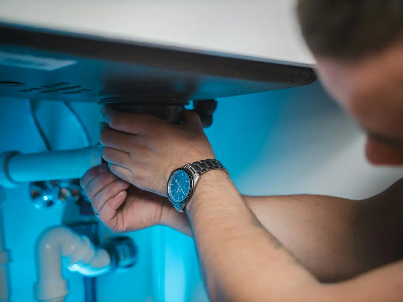 Hands tightening a drain fitting under a sink